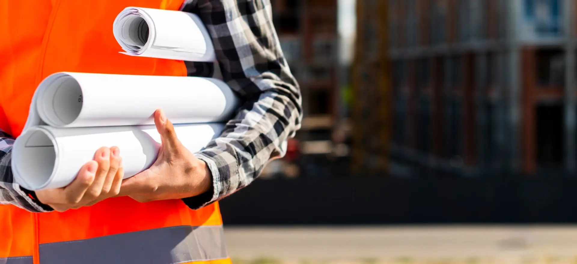 Engenheiro segurando plantas de projeto com estrutura metálica ao fundo